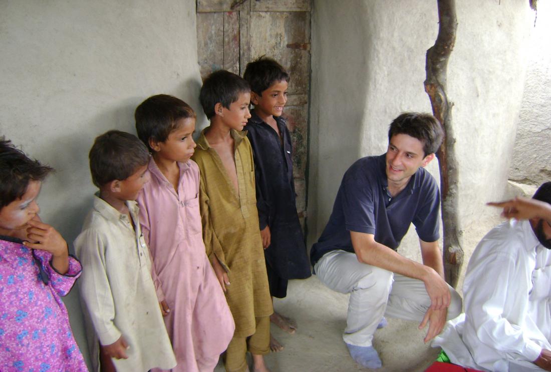 Children in shalwar kameez stand outside of mud building