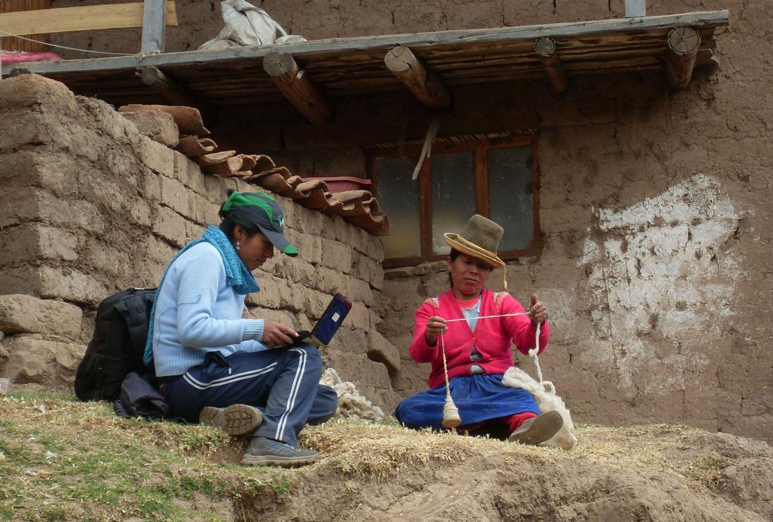 Woman on laptop talks to Peruvian woman spinning wool