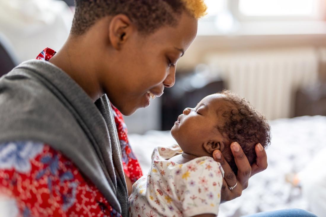 A smiling mother holds a young baby close to her, looking at the child.