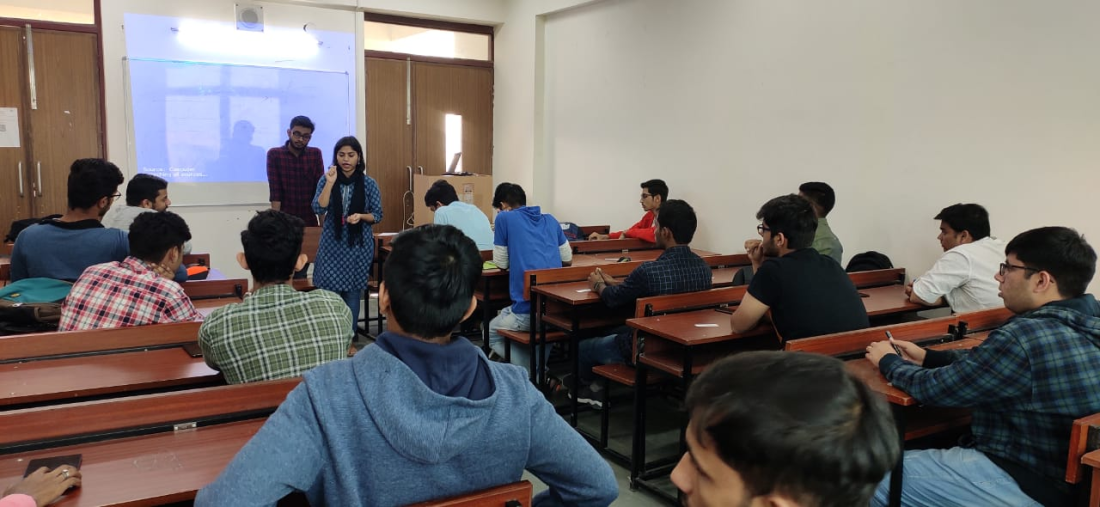 Students sit at desks in a classroom with facilitator at the front