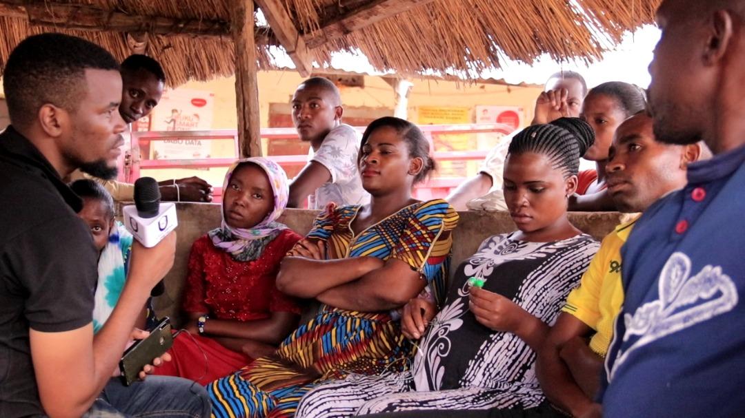 A journalist holding a microphone speaks with community leaders and citizens in Tanzania.