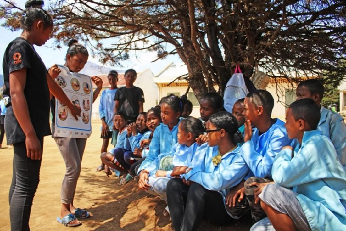 Adolescent girls holding a poster and talking to their classmates about menstruation in Madagascar