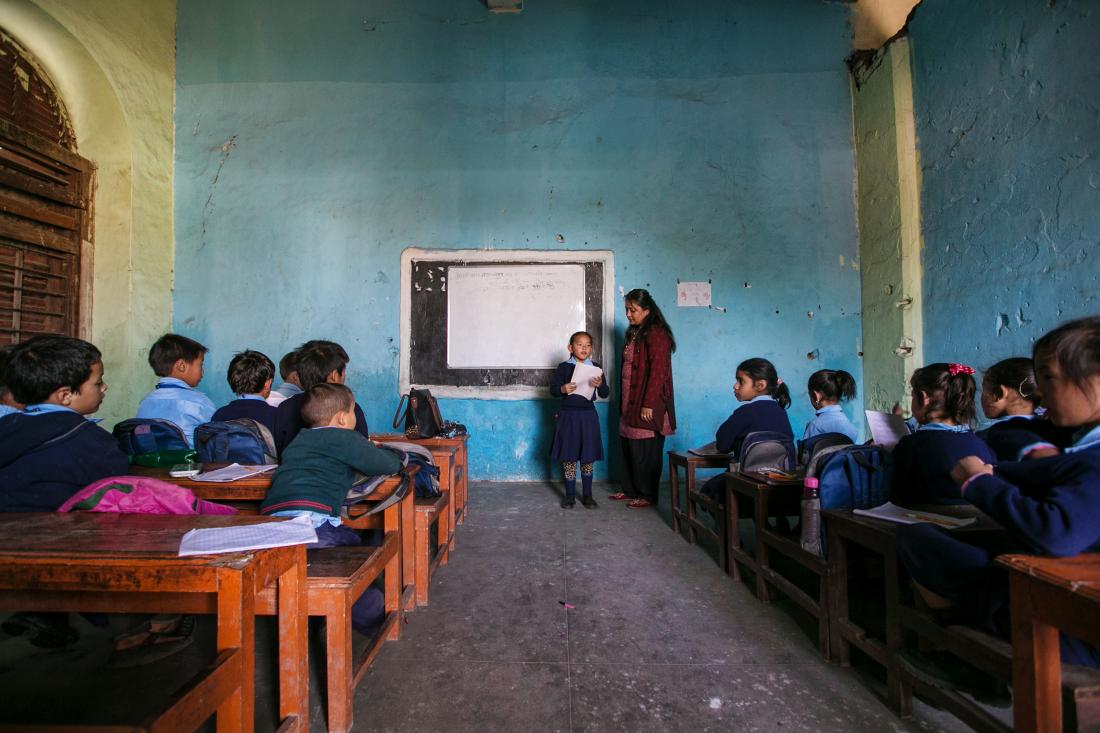 Students in a classroom facing the front where a teacher and student stand.