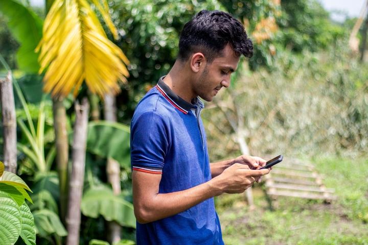 Man looks at his phone on a farm in Bangladesh.