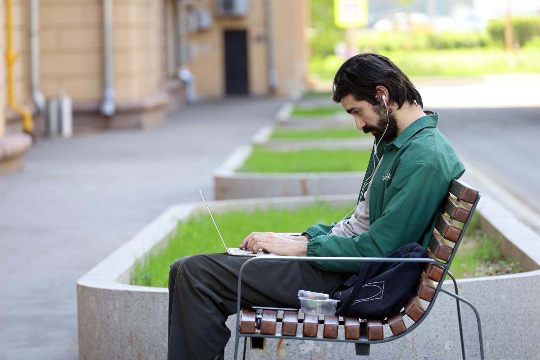 Man sitting on bench working on a laptop