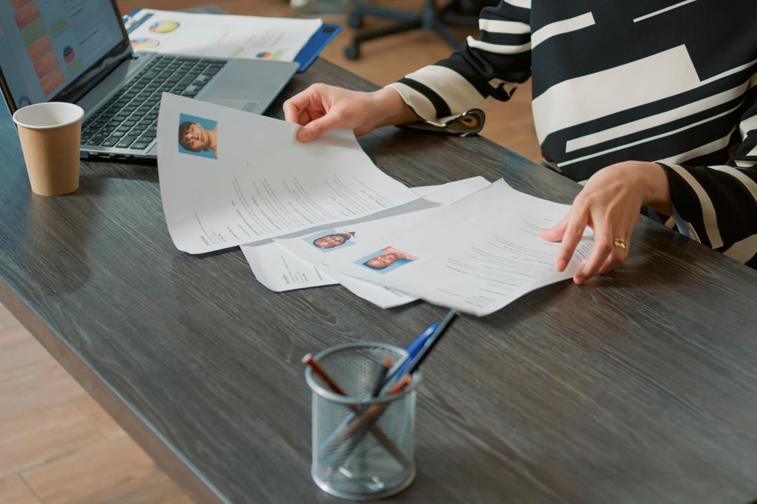 Recruiter reviews three resumes at a desk with coffee and a laptop