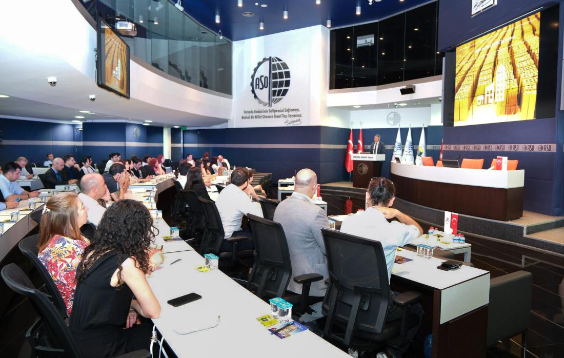 Firm representatives sitting in conference room for an event watching speaker at podium.