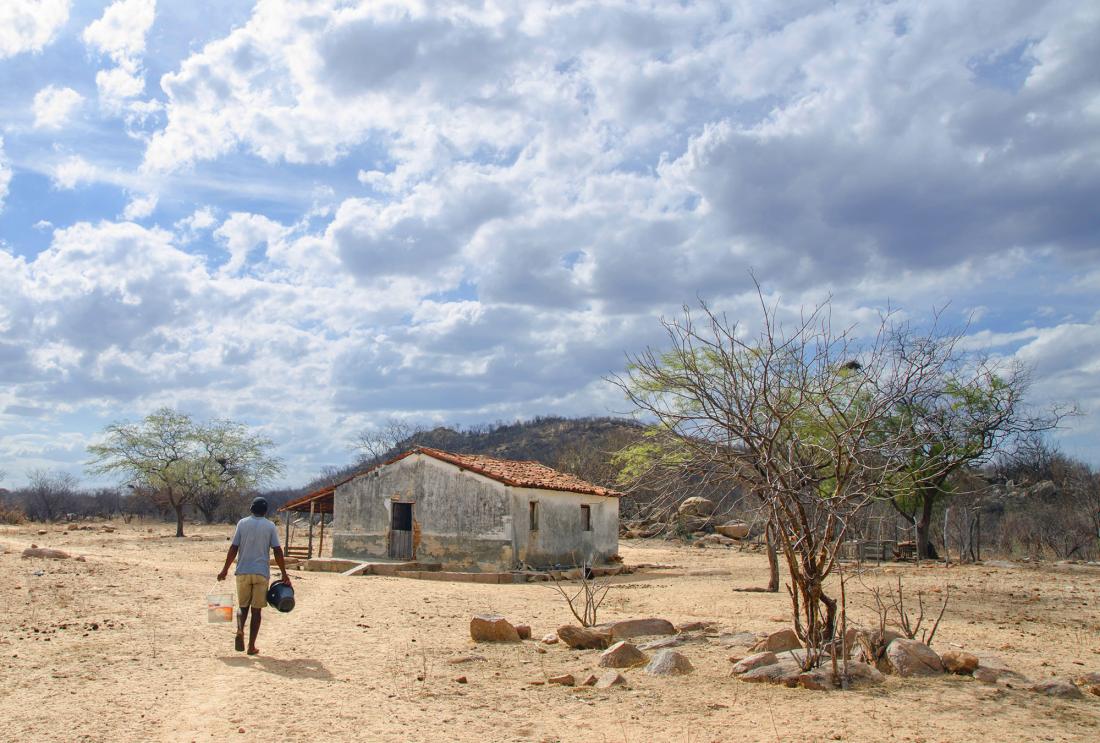 Man carries buckets of water to house in dry landscape