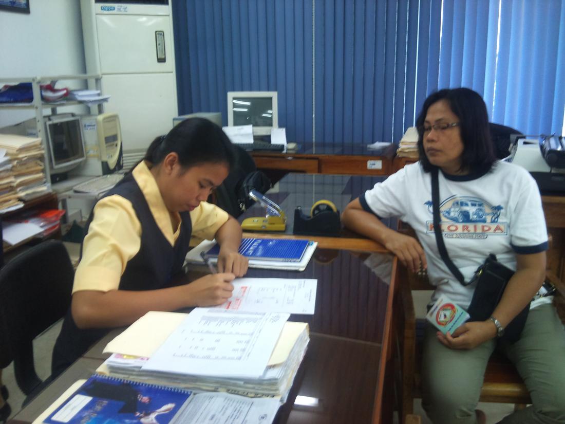 Woman writes on papers while woman looks on from across the desk