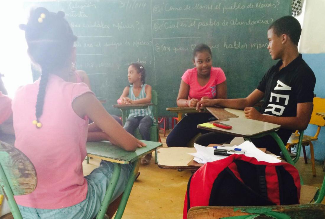 Children sit in schooldesks in front of blackboard