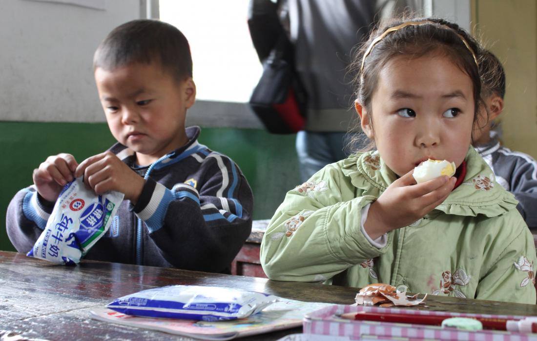 Young boy opening bag and girl eating egg