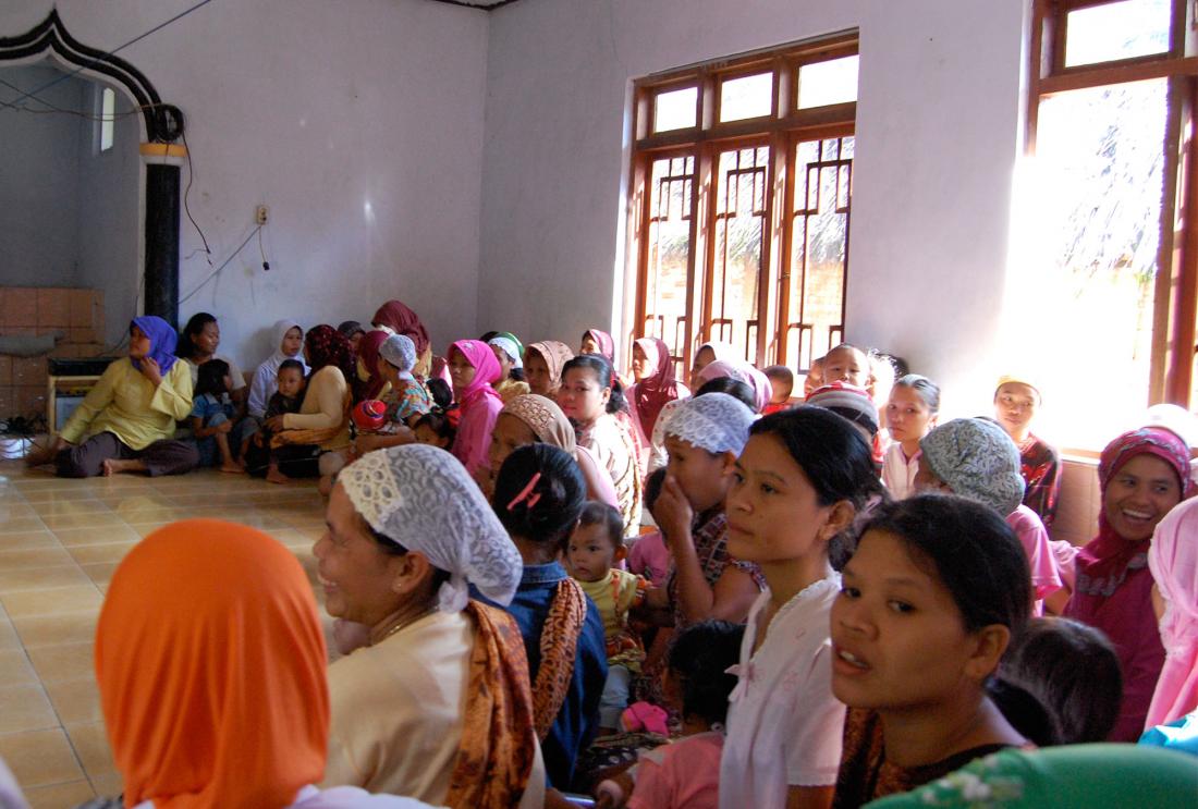 Large group of women wearing headscarves seated on wooden mat