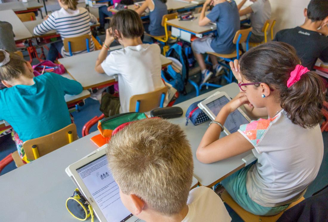 Children sit at desks looking at tablets