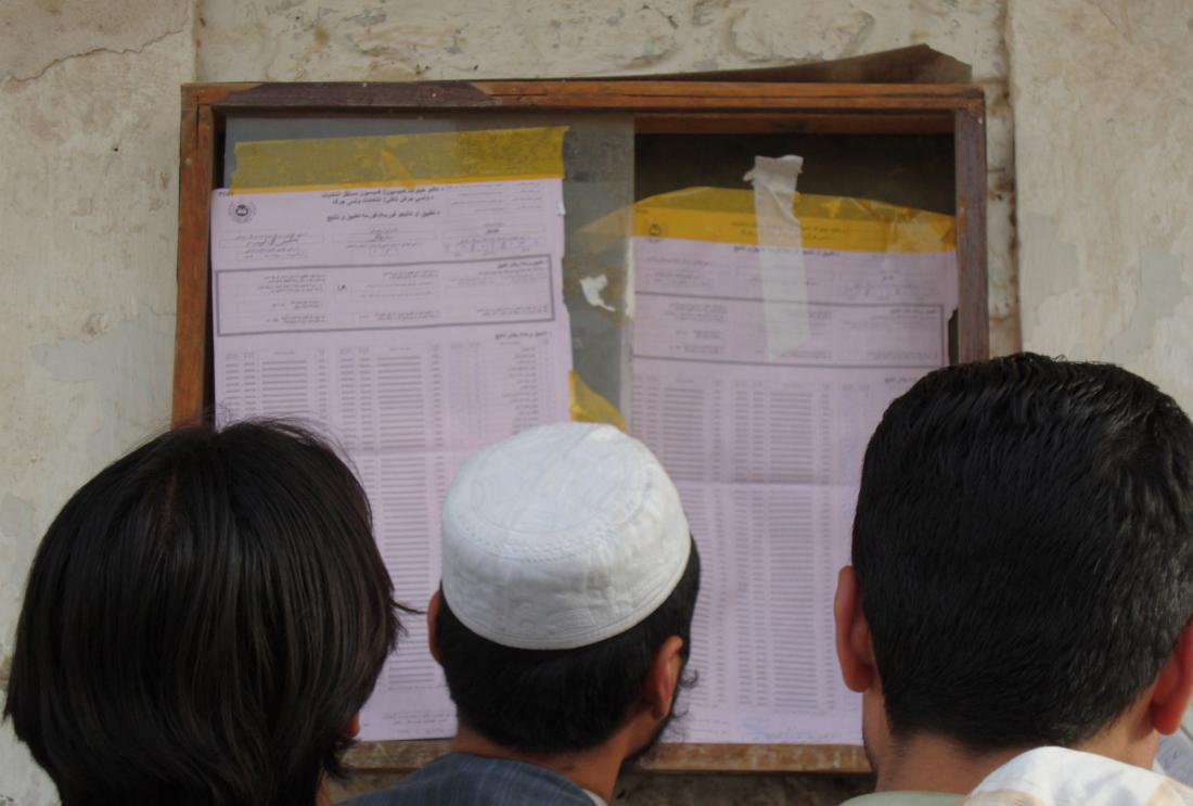 Back of three men's heads looking at papers taped to the wall