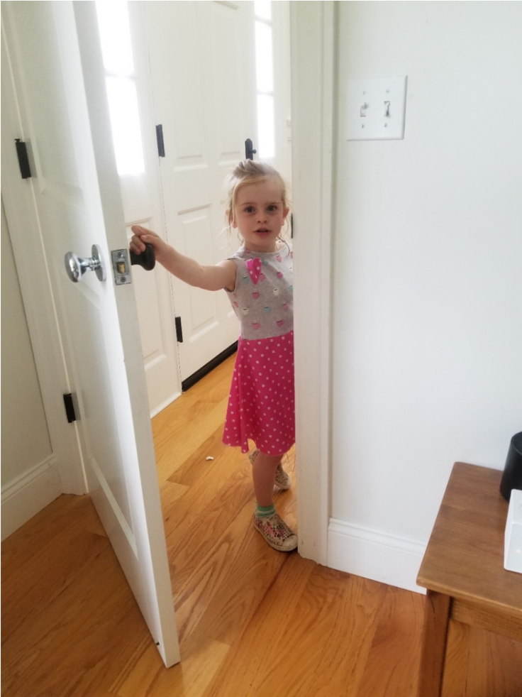 A young girl stands in an open doorway smiling at the camera