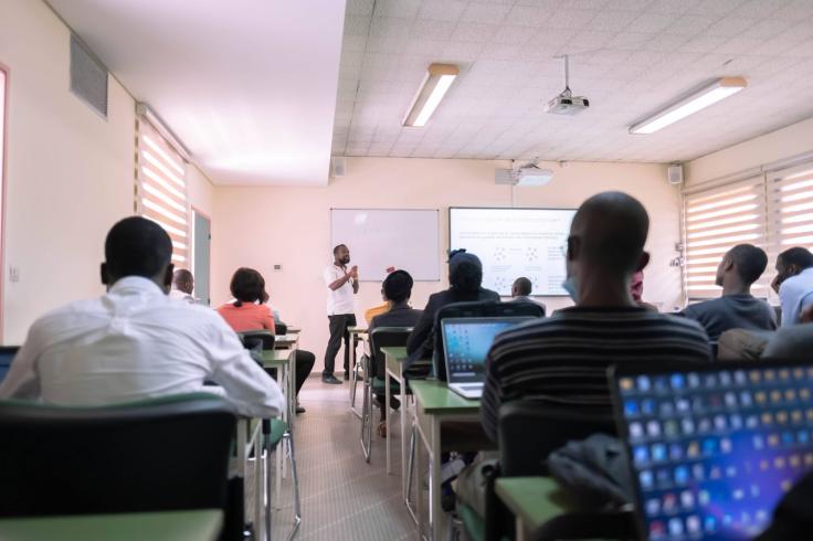 Individuals are pictured seated in a classroom observing a trainer presenting at the front of the room.