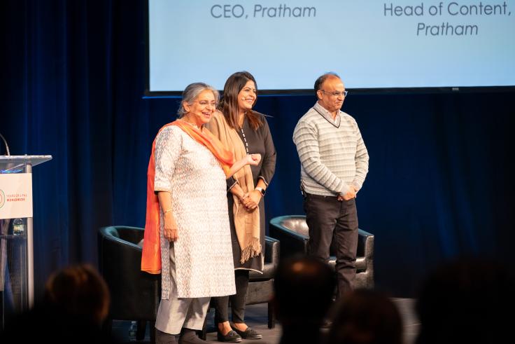 Two women and a man stand on a stage. 