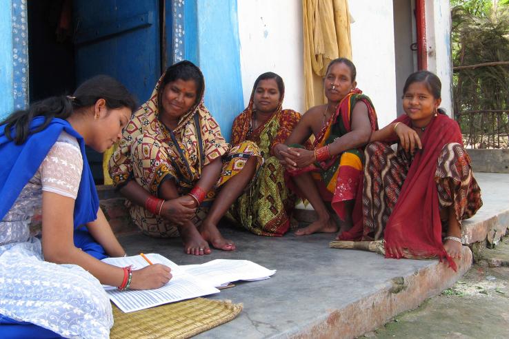 Group of women sit on an outdoor porch while a woman takes notes