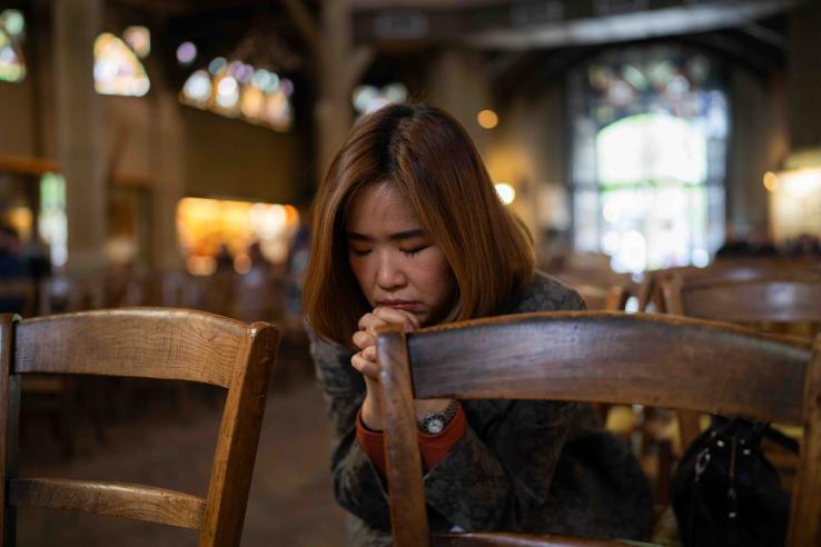 A woman bows her head in prayer while seated in a pew