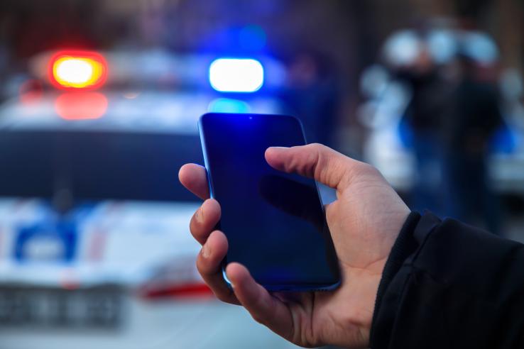 white hand holds cell phone with police cars blurred in background