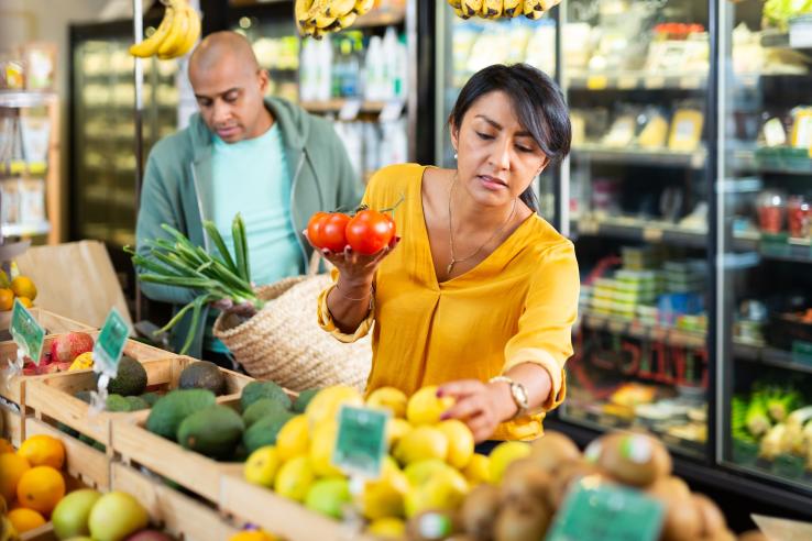 Woman (in foreground) and man (in background) picking out produce at a grocery store.