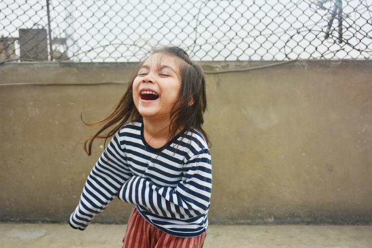 Preschool girl with long-sleeve striped shirt laughing with eyes closed in Colombia