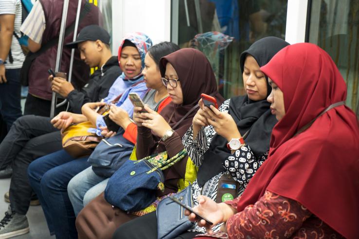 A group of female passengers look at public health campaigns on phones while sitting on a train in Indonesia.