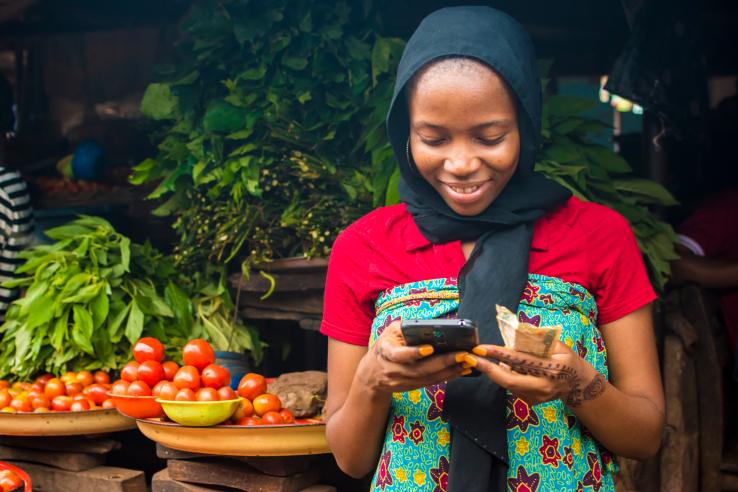 African woman selling in a local market while using her mobile phone.