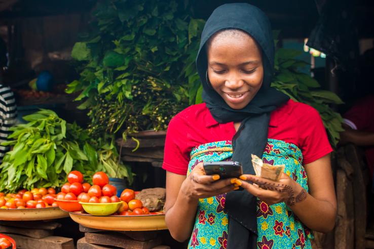 African woman selling in a local market while using her mobile phone. 