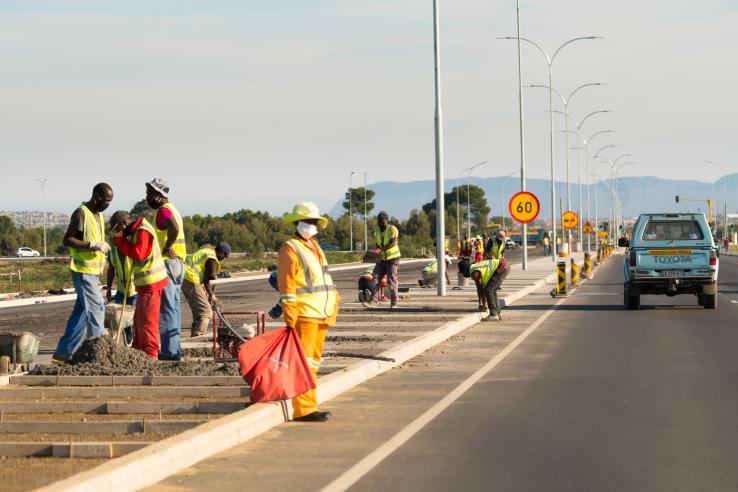 Workers construct a road while a car drives past on the right side
