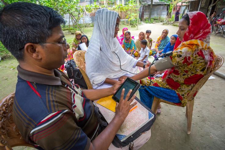 A man on the left checks a woman's vitals on the right while they both sit down.