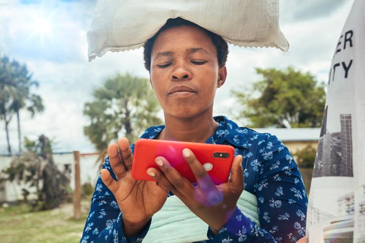 Village African woman carry a bag of rice on her head and is using the cellphone
