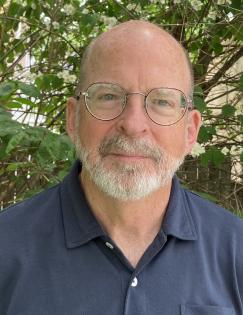 Head shot of a man with a blue shirt and glasses.