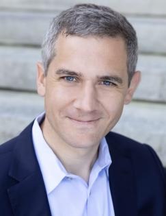a head shot of a man with short gray hair wearing a light purple shirt and navy blue blazer.