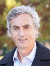 a head shot of a man with gray hair wearing a white shirt and a black jacket