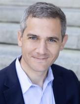 a head shot of a man with short gray hair wearing a light purple shirt and navy blue blazer.