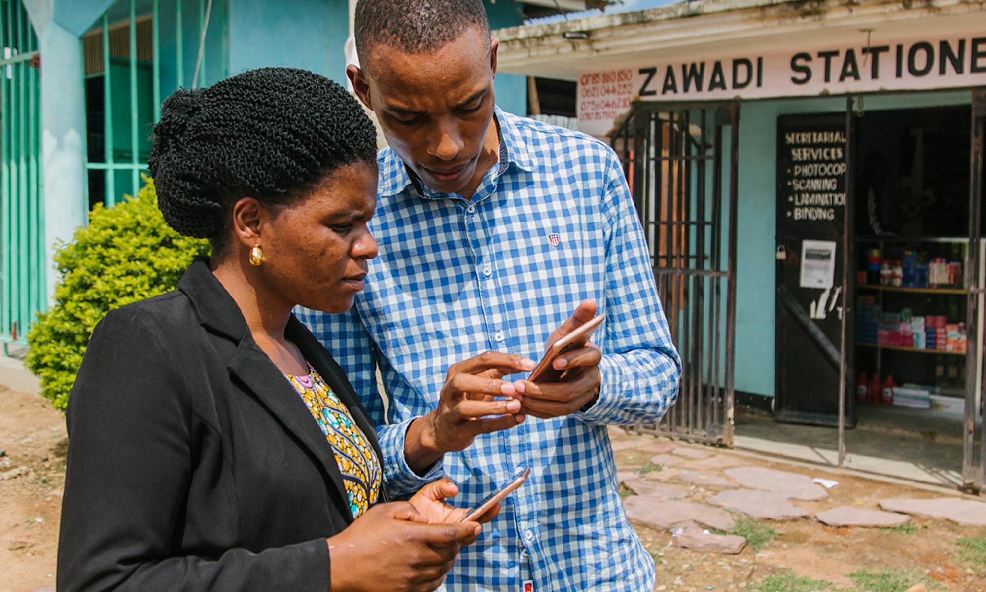 Man and woman standing in front of a store looking at their phones