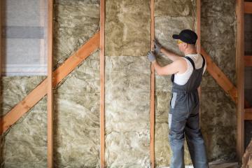 Man in overalls installs insulation between wood beams,