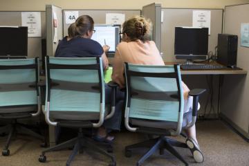 Two women sit before a computer screen.