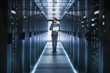 Man holding laptop walking through data center room 