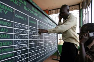 two men talking on phone and looking at blackboard containing table with numbers