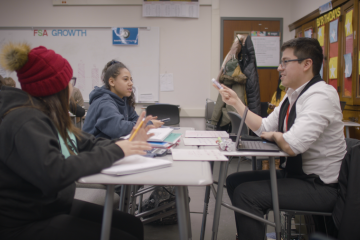 Teacher sitting across a desk from two students 