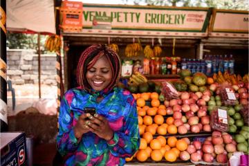 Woman uses mobile phone to make cash transfer in front of fruit stand