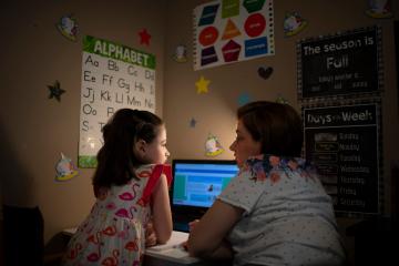 a teacher working on a computer with a young girl in a dim room