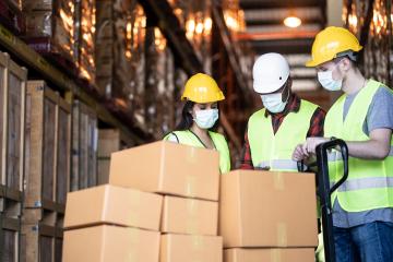 Workers in construction helmets stand around a stack of boxes.