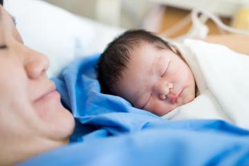 A mother and her newborn baby lay in bed together.