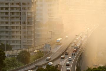 Cars and trucks drive on a highway in a city surrounded by smog