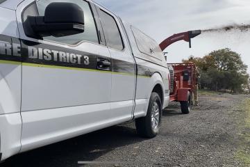 A woodchipper with 'Fire District 3' written on it working on by a road.