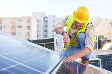 A man installs a solar panel on a rooftop on a sunny day.