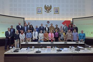 A group of men and women stand behind a conference table posing for a group photo. 